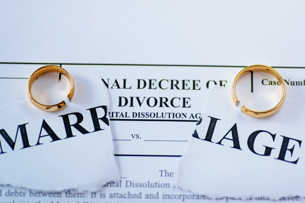 Ripped marriage papers with divorce papers under and two rings.