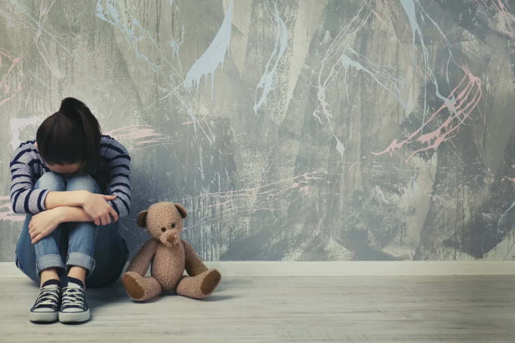 A young child siting on a floor with a stuffed bear next to her.