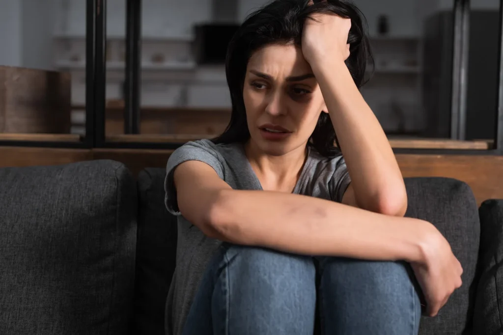 A distressed woman sitting on the floor with her hand on her head.