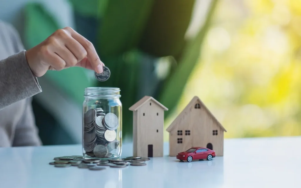 Two model homes on a table, and a person putting coins in a jar.